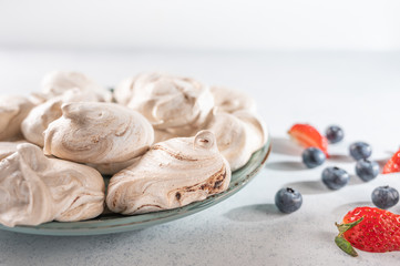 Homemade dessert meringue on a plate on light background. Napkin, strawberry and blueberry berries. Copy space