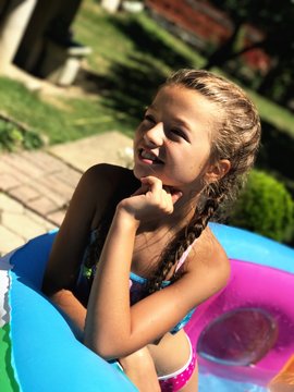 Smiling Girl With Hand On Chin Looking Away In Paddling Pool During Sunny Day