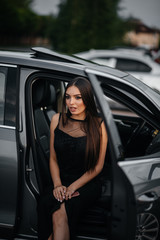 Obraz na płótnie Canvas Stylish young girl sitting in a business class car in a black dress. Business fashion and style