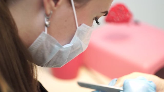 Professional manicurist masked girl manicures client in salon