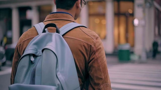 Handsome hipster guy with touristic backpack walking in downtown and using electronic headphones for listening music podcast from media website on cellphone, slow motion of millennial wanderer singing