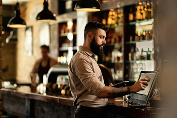 Young barista working at cash register in a bar.