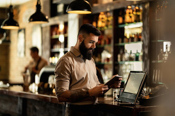 Young bartender using digital tablet while working in a pub. - obrazy, fototapety, plakaty