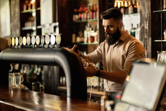 Young barista pouring beer from beer tap while working in a pub. - Powered by Adobe