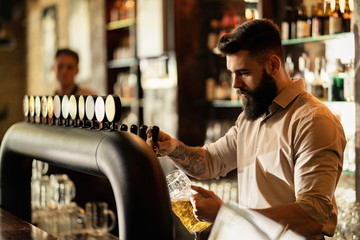 Young bartender pouring beer from beer tap while working in a pub. - Powered by Adobe