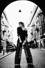 An attractive European girl posing in a street. She dressed in a dark clothes. Street photography. Black and white photo. Soft focus.