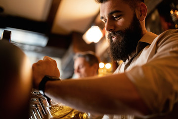 Below view of smiling bartender pouring draft beer in a glass.