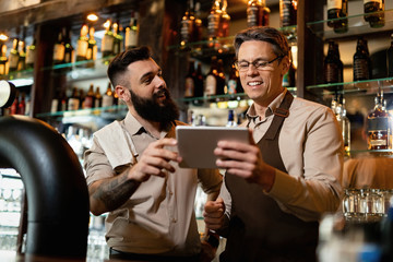 Happy bartenders using touchpad while working in a pub.