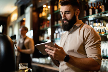 Young bartender using digital tablet while working in a pub.