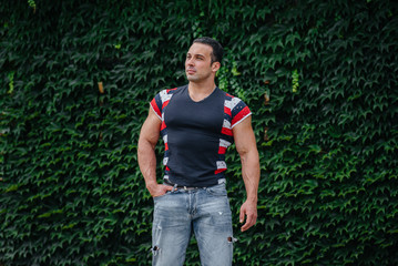 A sporty guy is sitting near a green wall of plants. Ecology