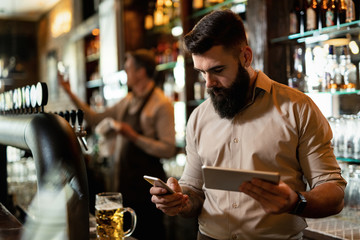 Young bartender text messaging on cell phone while working in a pub.