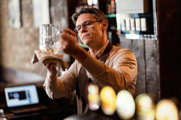 Barista cleaning drinking glass after working hours in a pub.