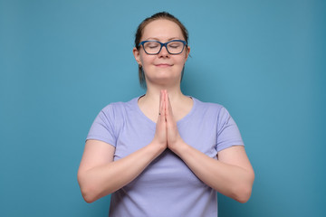 Mature caucasian woman in glasses holding hands together with eyes closed.