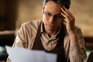 Distraught cafe owner reading reports while doing paperwork.