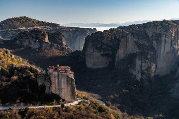 Aerial view of monastery Rousanou and breathtaking picturesque valley and landmark canyon of Meteora at sunset, Kalambaka, Greece, shadows, twisted road, bridge