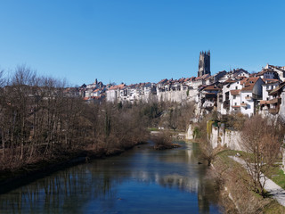 Fototapeta na wymiar View of the Sarine river and the Auge peninsula in Fribourg, Switzerland. Beautiful houses in the old city and the St-Nicolas cathedral on the right.