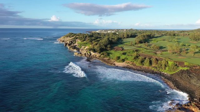 Low elevation aerial video of the southeast coast of Kauai with Lithified cliffs covered with ironwood pine trees, green golf courses and mountain range. #2 Poipu, Koloa, Kauai