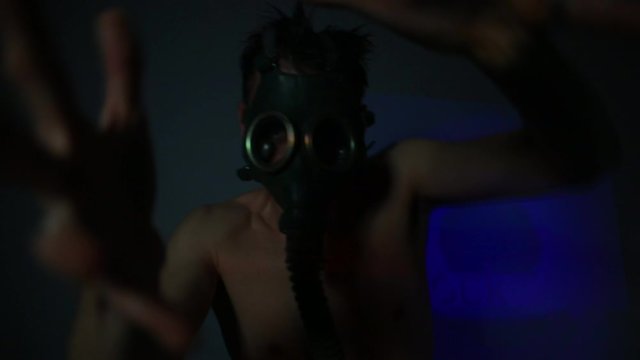 A man in a dark nightclub toilet dancing movements in a gas mask mask. Disco concept with DJ performance.