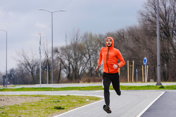 Handsome young athlete running fast in orange windbreaker jacket. Exercising, Jogging, Sport, Winter. Male athlete running.