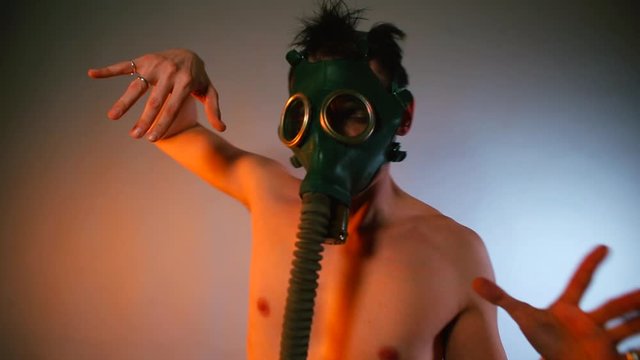 A man without a shirt and a gas mask on his face makes dance movements with his hands at a disco. Club dance party concept.
