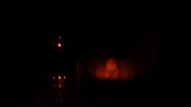 A closeup of a vacuum tube powering up in the dark. The scene starts completely black, then the tube slowly lights up as it gets hotter. Shallow depth of field, second tube in back very out of focus.