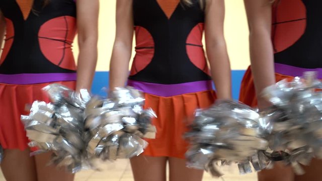 Athletic girls in cheerleader skirts uniform with pom poms support university sport team