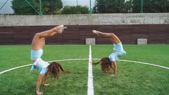 Two young girls in cheerleader in uniform support university sport team, making flip back
