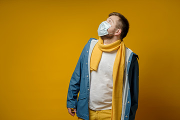 Man in a medical mask, in a scarf and jacket, fearfully looks upstairs, with copy space. Concept of the spread of the virus.