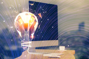 Computer on desktop in office with bulb icon hologram. Multi exposure. Concept of idea.