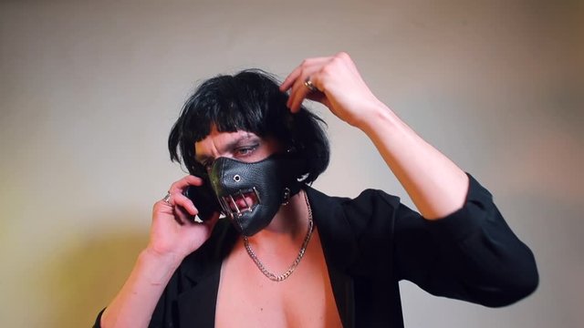 A masked man is talking on a cell phone during a BDSM session. The concept of telephone dependence, nomophobia