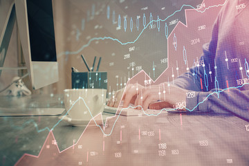 Multi exposure of graph with man typing on computer in office on background. Concept of hard work.