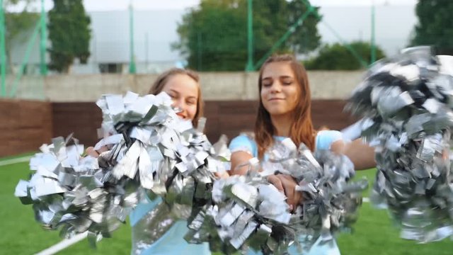 Teenage girls in cheerleaders in uniform shaked with pom poms, support university sport team