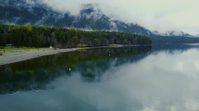 Cloudy mountains and fly over the lake towards the beach with the forest around