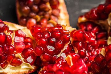 Broken red ripe pomegranate fruit on the dark rustic background. Selective focus. Shallow depth of field.