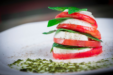 Ensalada Capressa Tomate queso albahaca y pesto en plato blanco