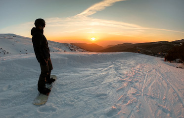 Person practicing snowboarding, stops to watch the beautiful sunset.