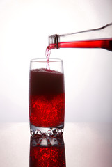 Pouring a refreshing red bubbly soda drink from bottle into glass on white background closeup with reflections