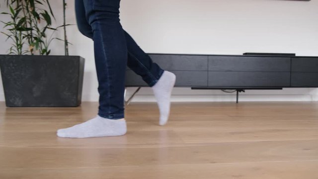 Woman feet in geans and socks walking across modern living room interior - tracking closeup shot