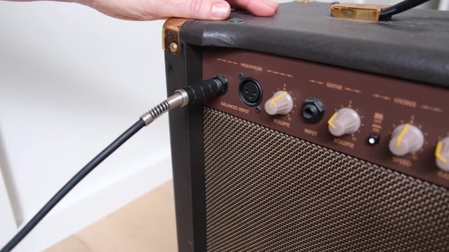 Woman hands plugging guitar cord into acoustic amplifier and adjusting volume knobs