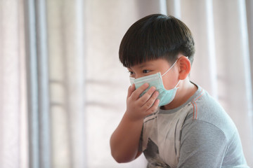 Portrait of little asian boy wearing mask sitting in room for protect pm2.5 and stop corona virus outbreak. Coronavirus and Air pollution pm2.5 concept.