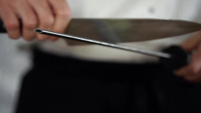 Chef in white uniform and black apron sharpening big Japanese knife with diamond covered steel stick, SLOW MOTION
