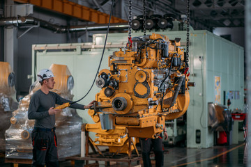 A worker in a helmet attaches locks to the engine to lift it on a crane.