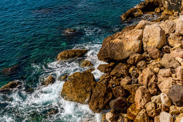 A close-up shot of the Mediterranean Sea turquoise water and powerful waves beating against the rocks on the coast