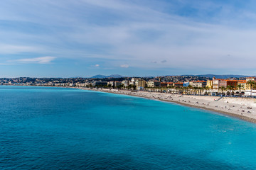 Naklejka na ściany i meble Panoramic wide angle shot of the Quai des États-Unis, people relaxing on the beach of the Mediterranean Sea coastline with the sunlight reflecting in the turquoise water (Nice, France)
