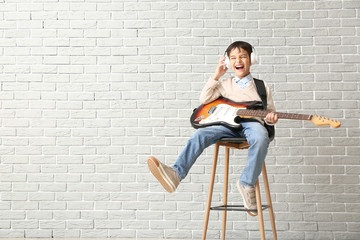 Fototapeta premium Little boy playing guitar against brick wall