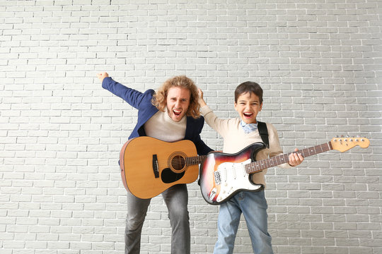 Emotional man and his little son playing guitars against brick wall