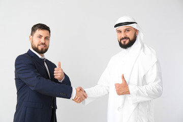 Arab man and his business partner shaking hands on grey background