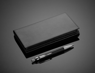 Fashionable leather men's wallet and pen on a black background