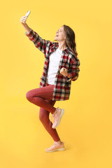 Happy young woman taking selfie on color background