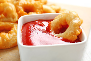 Crispy fried onion rings and tomato sauce on table, closeup